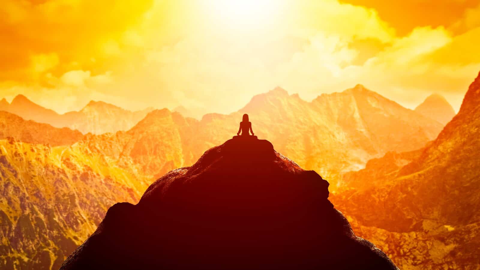 meditating silhouette on top of mountain with sun backdrop